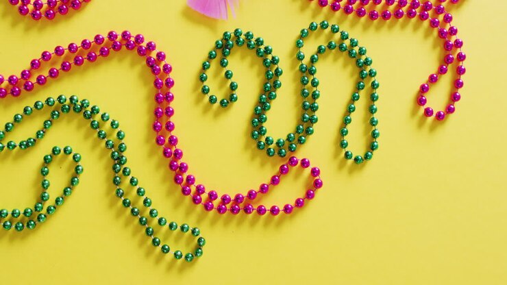 Video of pink mask, with mardi gras beads and feathers on yellow background with copy space