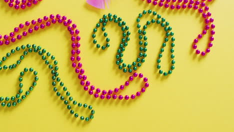 video of pink mask, with mardi gras beads and feathers on yellow background with copy space