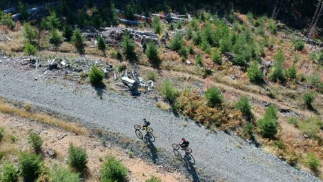 drone footage of 2 people on mountain bikes ridding up the road on a beautiful summer day in the pacific northwest