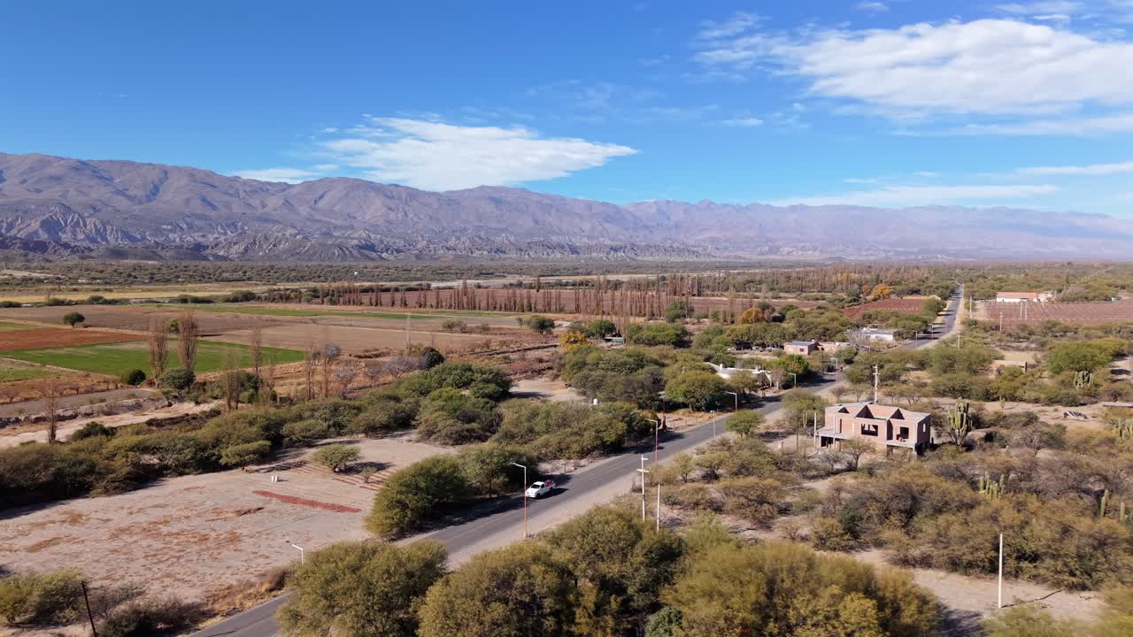 Drone con tracciamento a sinistra si muove verso vasti vigneti, case rurali e un'ampia distesa di terra con montagne sullo sfondo durante una giornata di sole