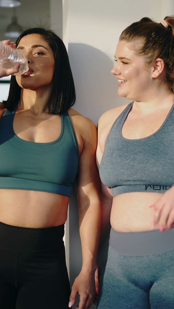 Vertical video: Drinking left woman in sportswear sipping bottle after gym, friend wiping sweat