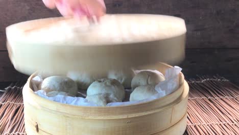 three quarter view of uncovering lid of cooked steamed buns showing steam rising