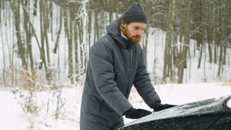 uomo che chiude il cofano dell'auto dopo aver controllato il motore ed essere entrato in auto durante una giornata invernale nevosa