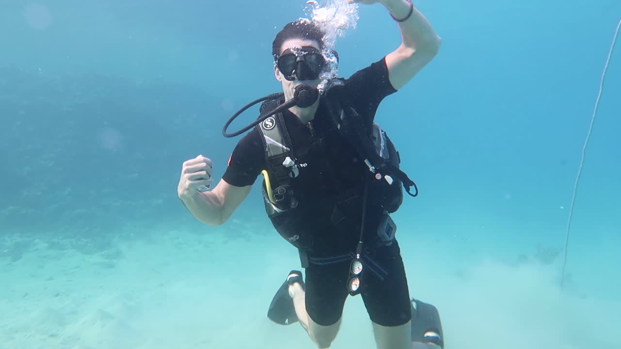 un joven buzo caucásico completamente equipado haciendo payasos bajo el agua como un hombre fuerte