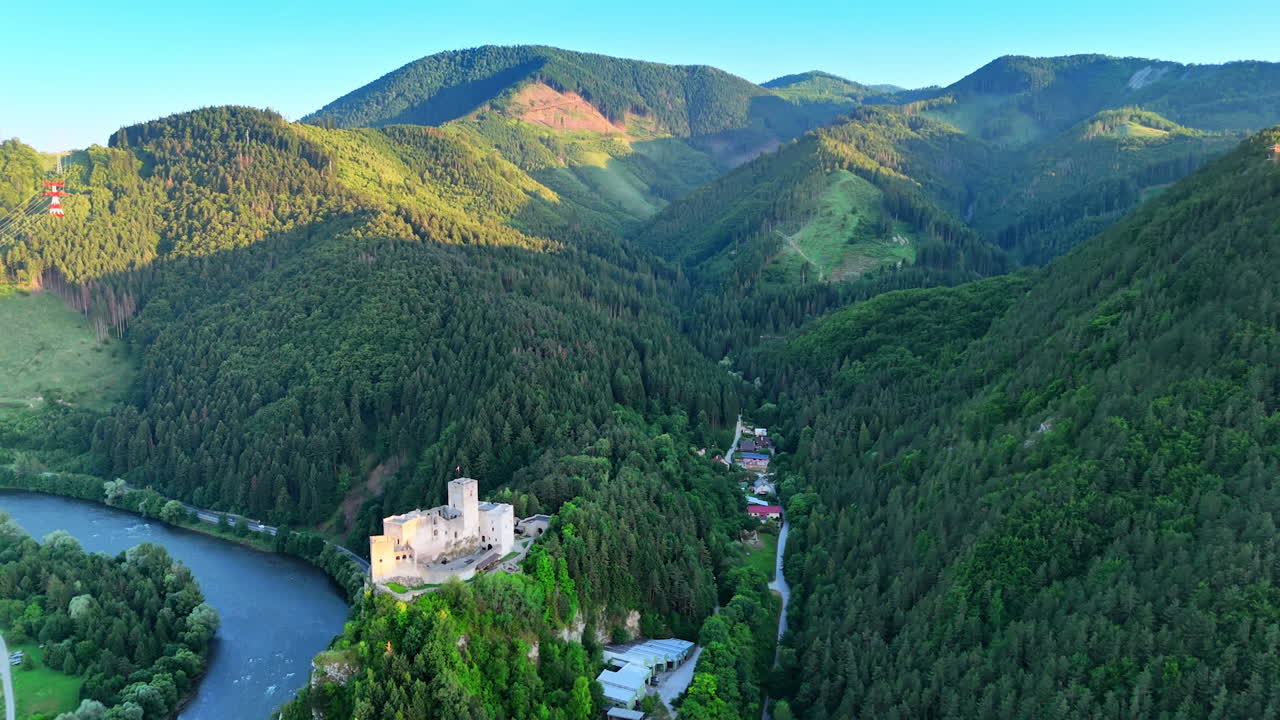 Tatra mountains covered with lush green pine tree forests in Slovakia. Drone footage approaching the Strecno Castle on the rock over the river