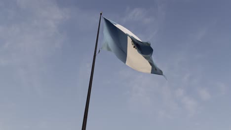 the guatemalan national flag gracefully waving atop a tall flagpole, set against a clear blue sky on a windy day.