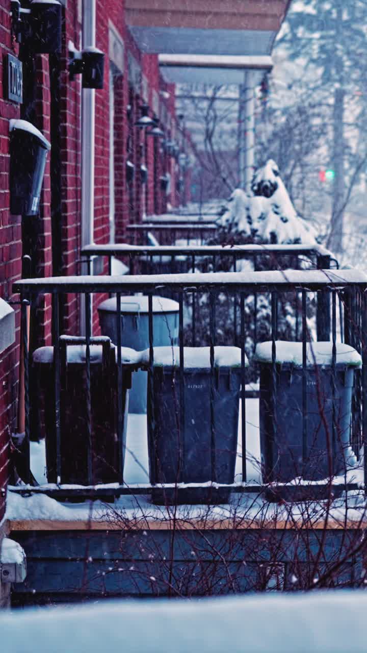 Snow covered balconies and brick apartments in winter storm with snow accumulating on trash refuse bins, vertical backdrop