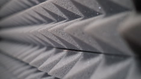 primer plano íntimo de paneles de espuma acústica en forma de pirámide gris, capturando la textura y los reflejos de luz ideales para configuraciones de audio profesionales