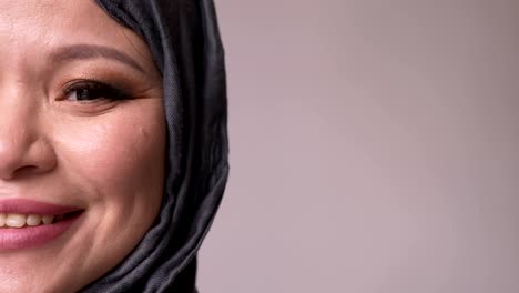 closeup half-face shoot of adult attractive muslim female in hijab looking forward and turning to camera smiling happily with isolated background