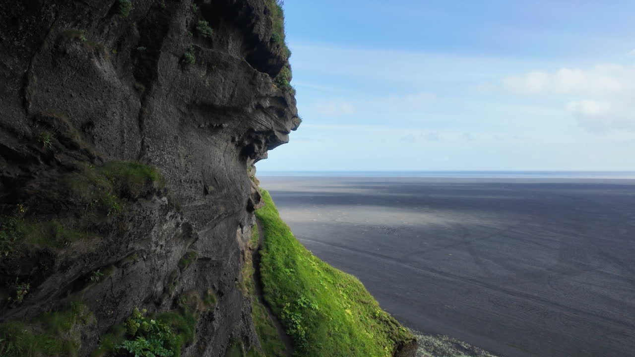 Beautiful natural scenery of Icelandic cliffside with green moss and vast black sand plain stretching to horizon, Iceland