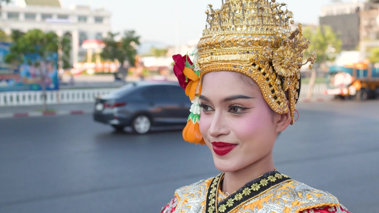 Nærbillede af en Thai Khon-danser i udsmykket kostume, stående foran en bygade.