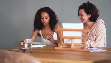 mujeres diversas sentadas en la mesa con pincel de pintura y colores de agua