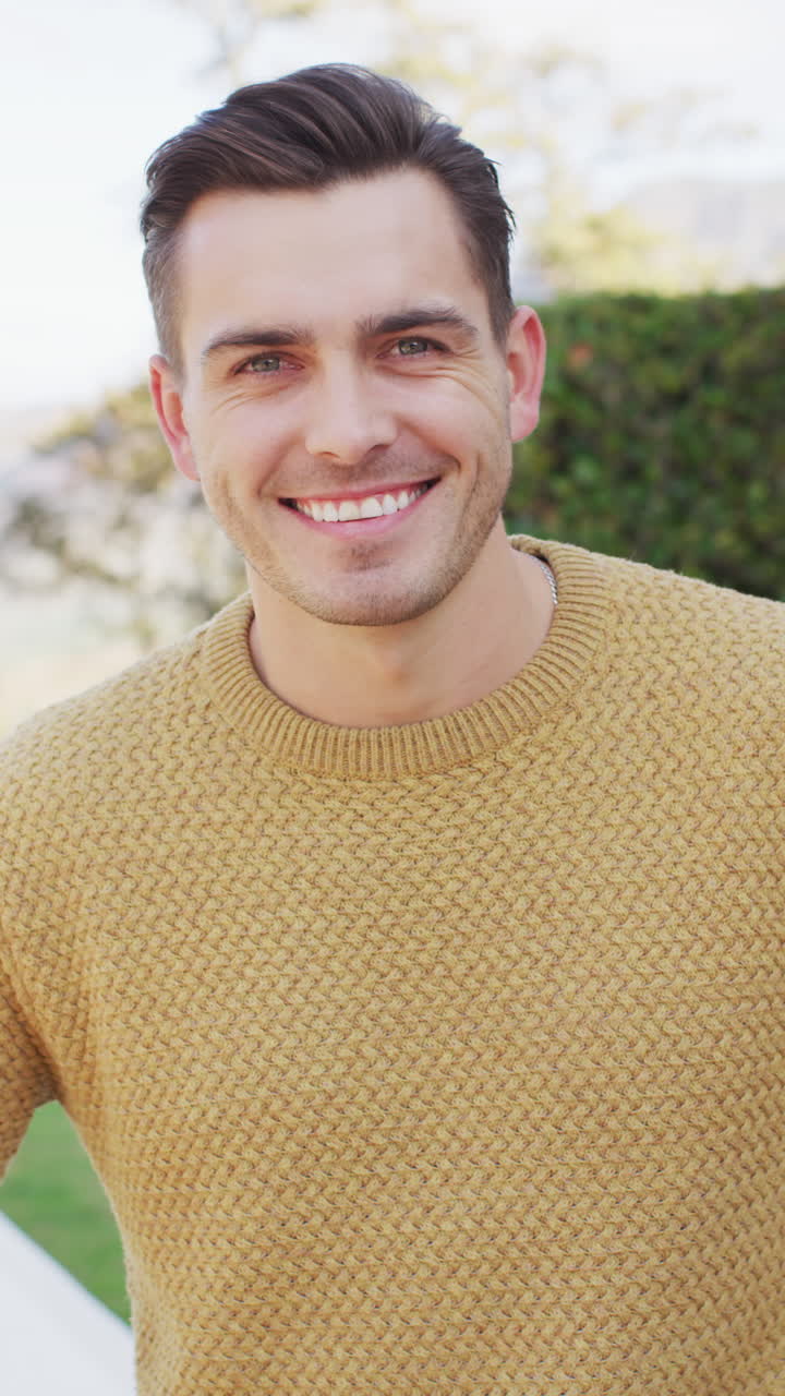 retrato de video vertical de un hombre caucásico feliz con cabello corto sonriendo a la cámara en el jardín