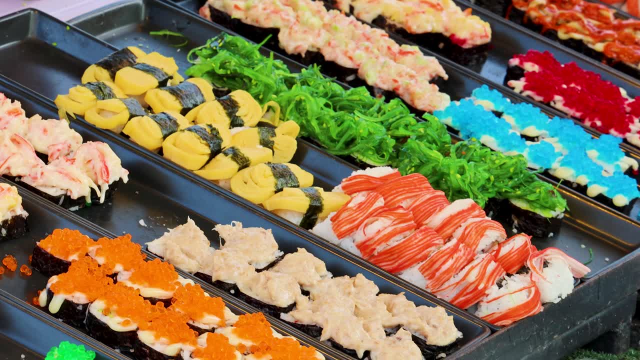 Hand choosing assorted sushi from vibrant display under natural daylight at traditional food stall