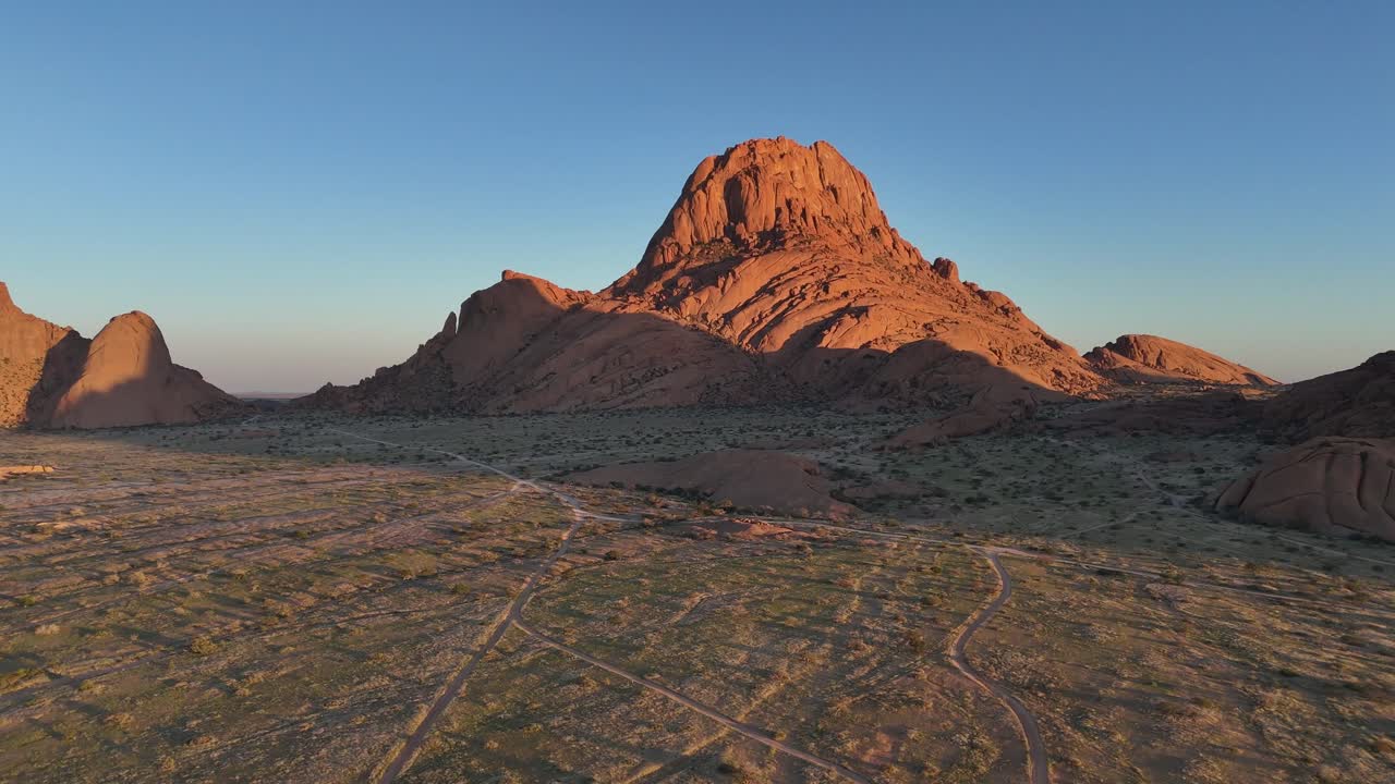 Sweeping aerial over the Spitzkoppe landscape, showing endless desert plains and iconic rock outcrops under a deep blue African sky