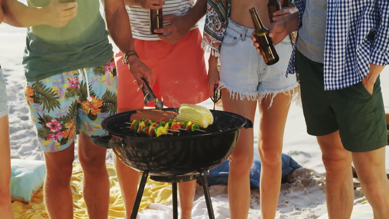 amigos cocinando comida en la barbacoa y bebiendo cerveza en la playa 4k
