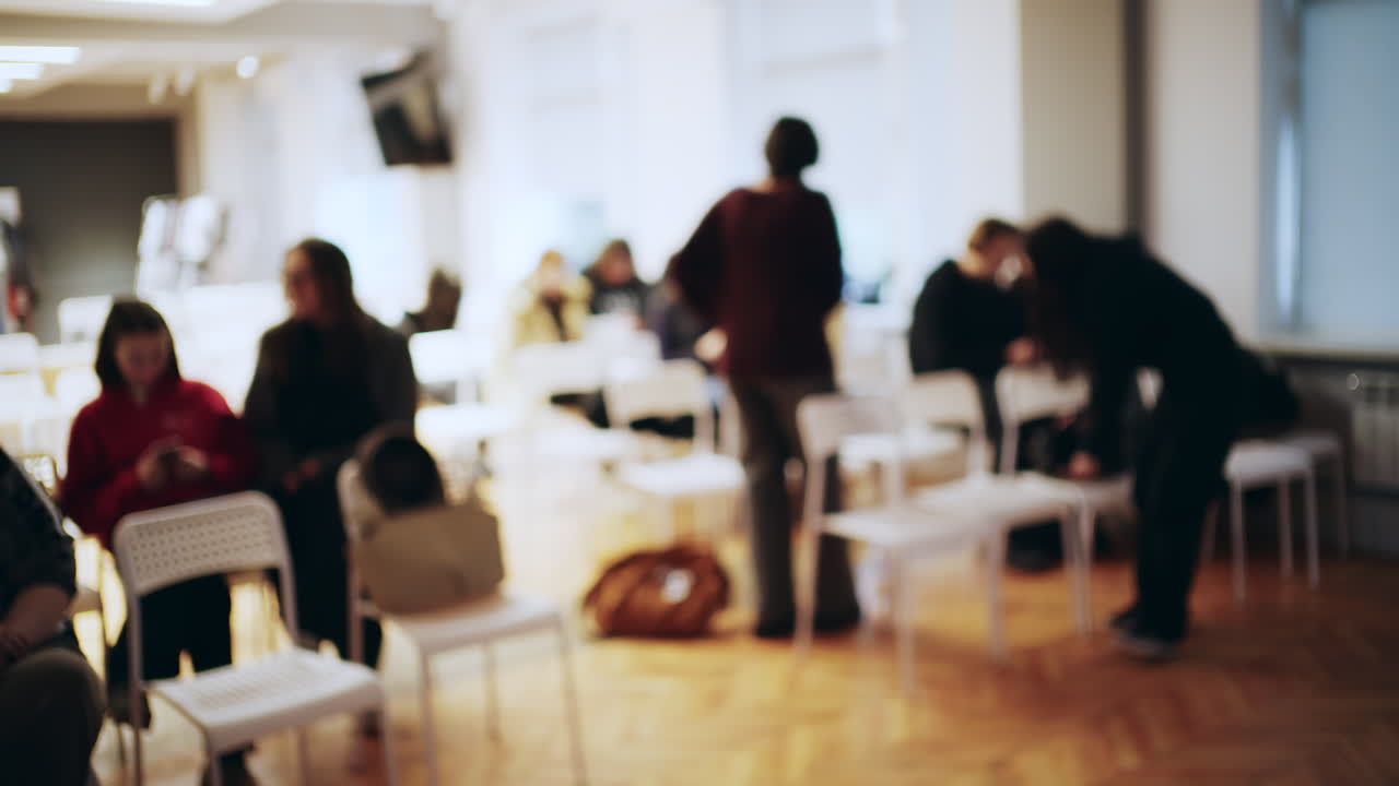 Scatto sfocato di persone che si radunano e siedono su sedie in una luminosa sala conferenze o workshop.