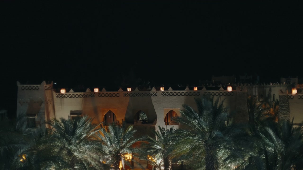 Mura illuminate della kasbah con portali ad arco e palmeto di notte in una città oasi marocchina