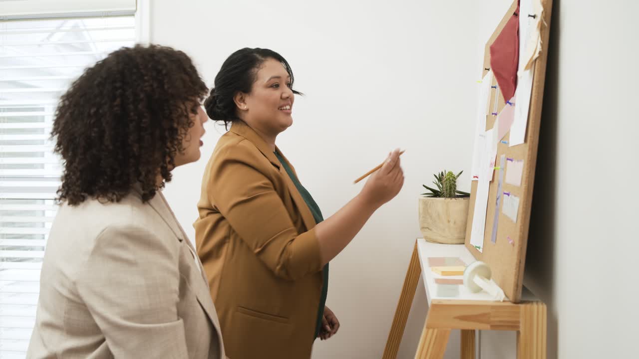 Diverse female coworkers in studio holding swatch pointing at mood board sketching to refine design