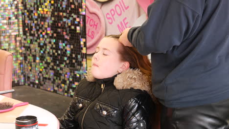 a young girl with closed eyes enjoys having her hair platted styled in plats in a salon