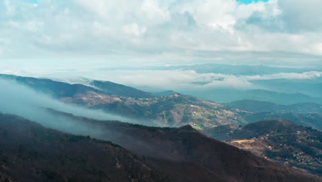 Misty-mountain-landscape-with-sunlit-valleys-and-cloud-covered-peaks,-aerial-view