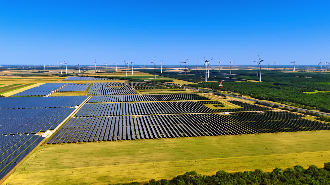 Numerous solar panels gather sunlight in the fields. Wind turbines produce green energy. Aerial view