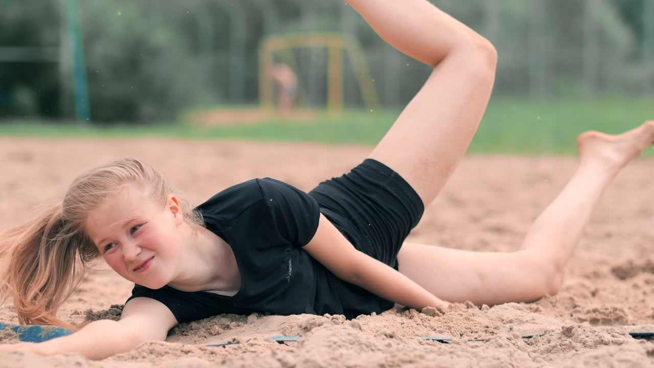 Young female athlete dives into the sand and saves a point during beach volleyball match. Cheerful Caucasian girl jumps and crashes into the white sand during a beach volley tournament.