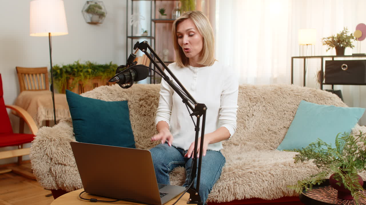 Voksen kvinne spiller inn en online podcast-vlogg hjemme med studiomikrofon, gestikulerende mens hun snakker