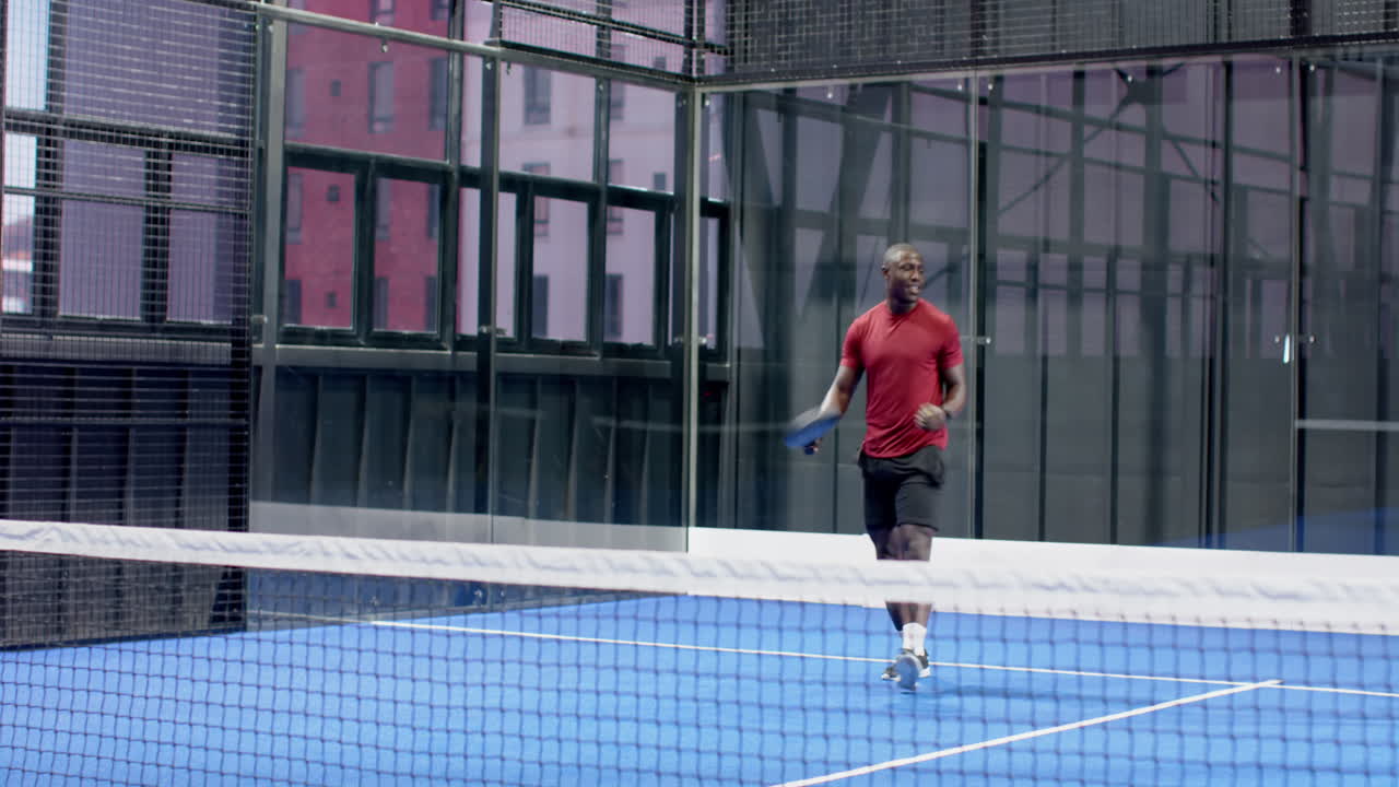 African American man playing padel tennis, hitting ball with focus and energy, at indoor court