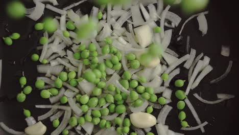 slow motion close up top view of peas poured into a pan with oil, onion and garlic with bokeh effect. mediterranean home made cooking