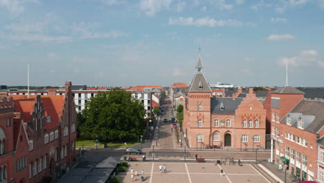 Aerial-view-backwards-of-Torvet-square-in-Esbjerg,-Denmark-with-the-statue-of-Christian-IX-and-the-Town-Hall.-Establishing-drone-view-of-the-historical-city-centre-with-lot-of-tourist-and-pedestrians
