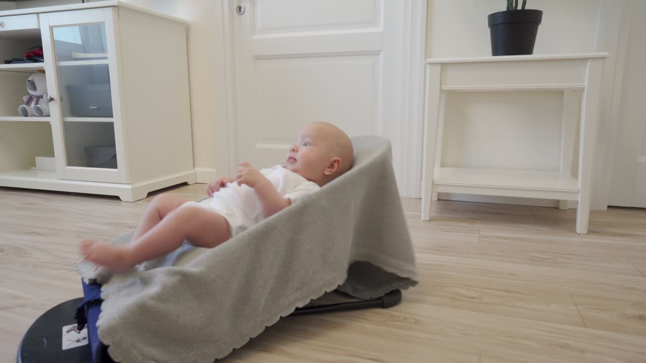 Aspirapolvere robot che esegue la pulizia automatica dell'appartamento, muovendosi intorno a un bambino su una sedia a dondolo; moderna tecnologia di pulizia intelligente.