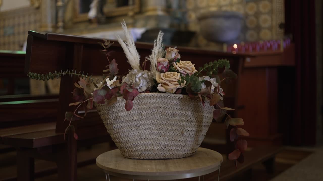 cesta rústica llena de flores y vegetación colocada en un soporte dentro de una iglesia