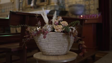 ein rustikaler korb, gefüllt mit blumen und grün, der auf einem stand in einer kirche platziert ist