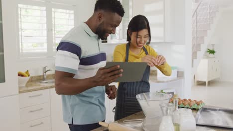 Happy-diverse-couple-using-tablet-and-baking-in-kitchen