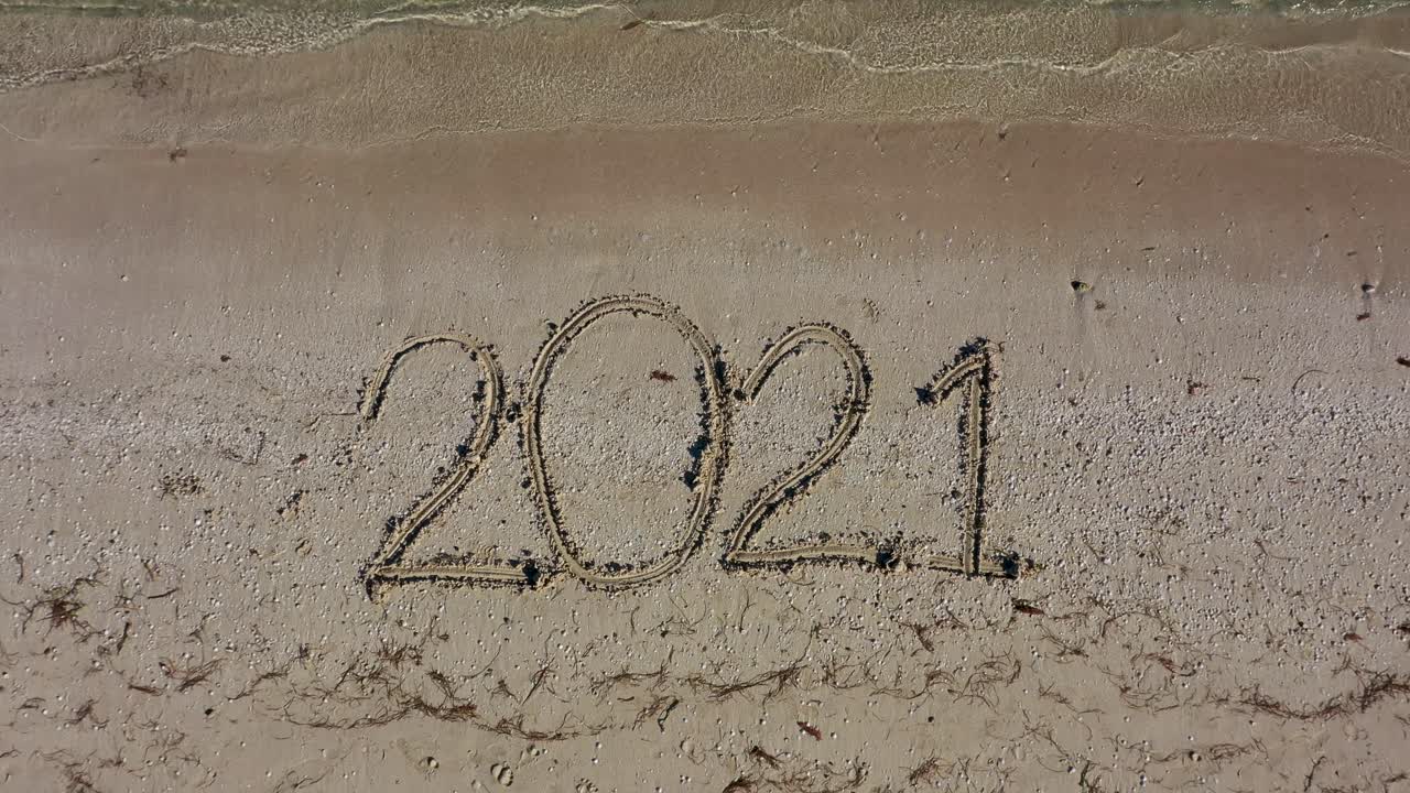 veintiuno escrito en la arena llena el marco y se hace más pequeño a medida que la cámara se aleja manteniendo la fecha en el centro del marco