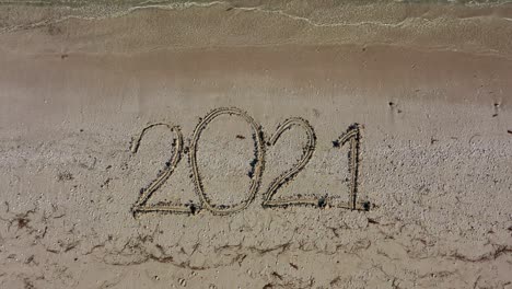 twenty twenty one written in the sand fills the frame and gets smaller as the camera moves away keeping the date in the middle of the frame