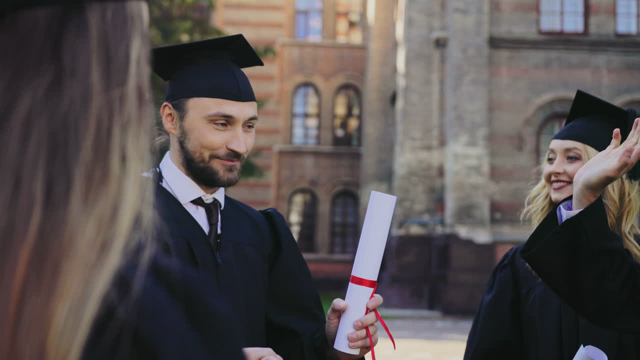 Caucasian male and female graduates holding their diplomas and talking after the graduation day at their University building