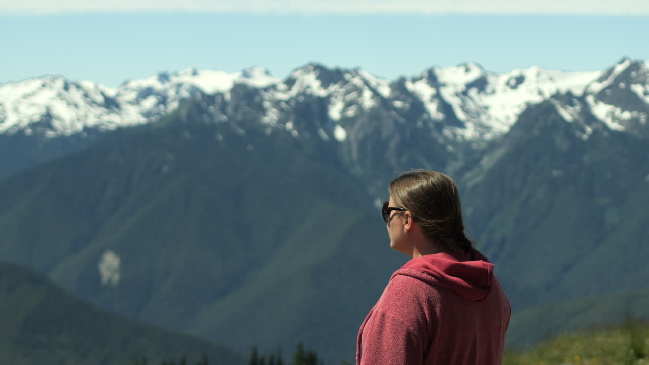 Kvinde i lyserød jakke ser på sneklædte Hurricane Ridge-bjerge