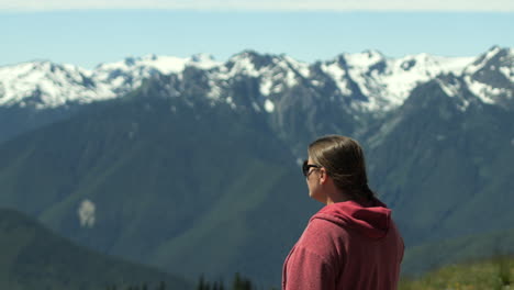 woman wearing pink jacket looking at snow capped hurricane ridge mountains