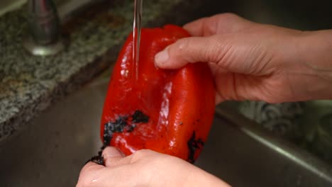 removing roasted skin of red bell pepper in tap water. close up