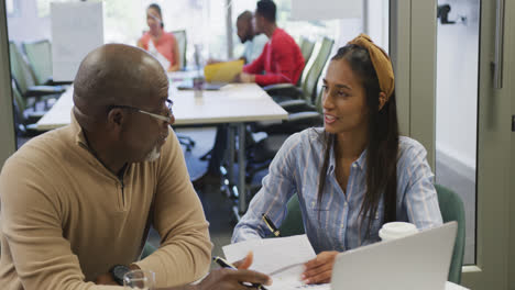 Diverse-male-and-female-business-colleagues-talking-and-holding-documents-in-office