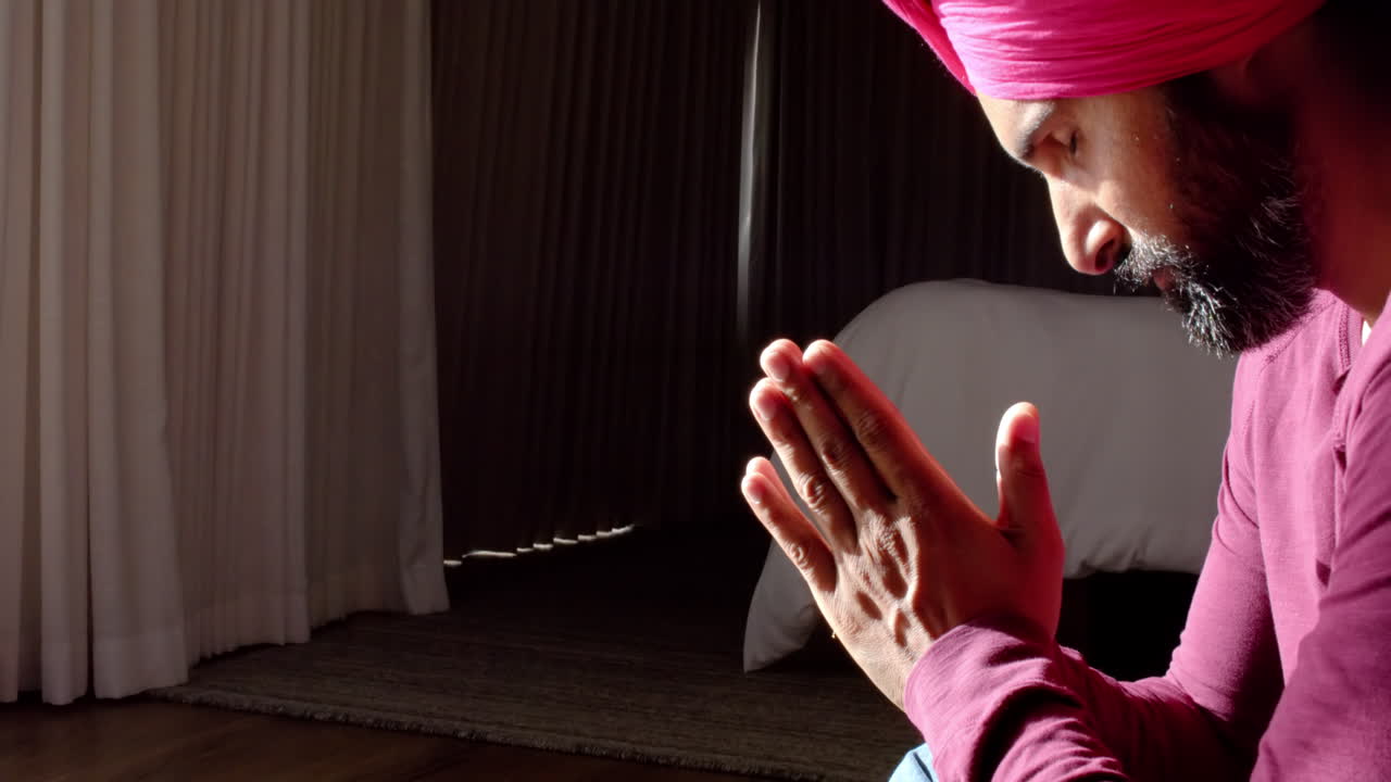 Praying with hands together, man in traditional attire sitting indoors