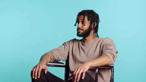 bored man in wheelchair impatiently tapping fingers, studio background