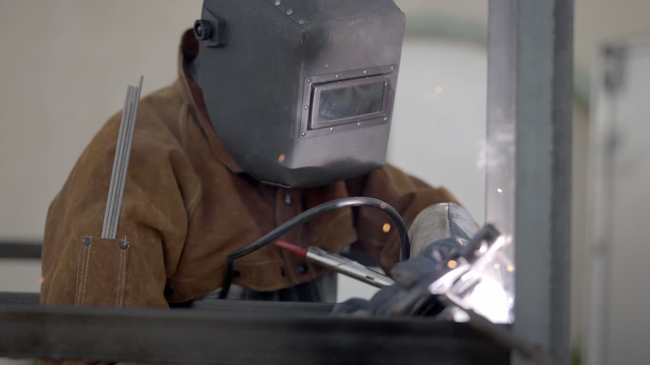 Welder welding metal construction in workshop- sparks shield mask circle pan