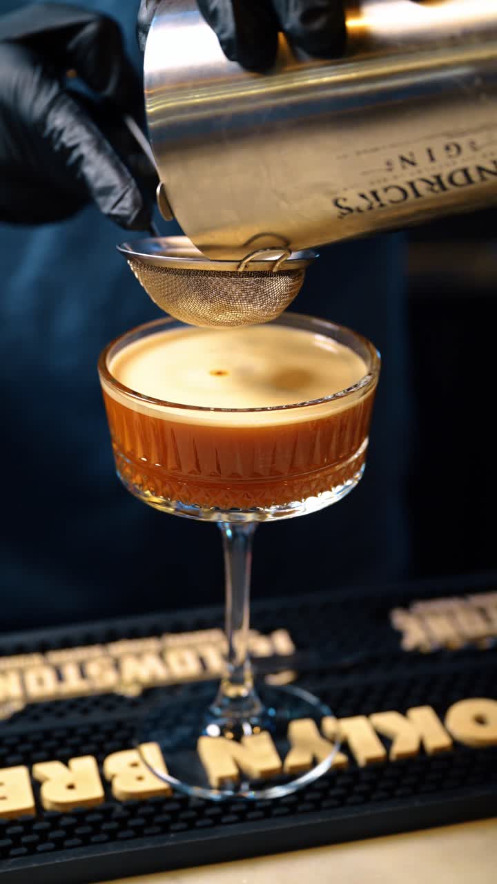 New York, USA, 15 aprile 2026: Filtrare un cocktail espresso martini in un bicchiere coupe ghiacciato. Primo piano di liquido marrone che scorre attraverso un colino a maglie fini in un bicchiere di cristallo