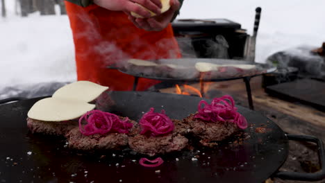 close up male grilling reindeer burger on barbeque with cheese and red onion toppings, sweden