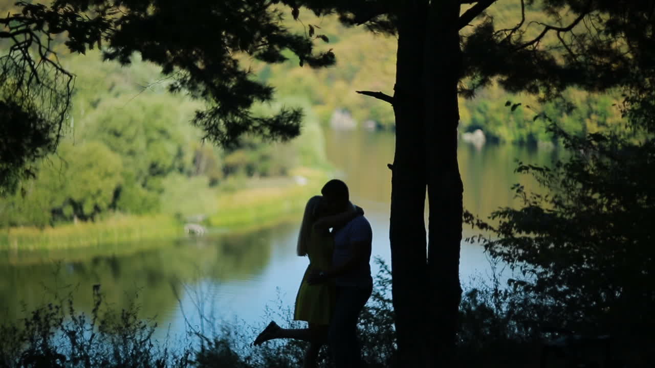 Silhouette of young couple. Silhouette of kissing couple in forest near river