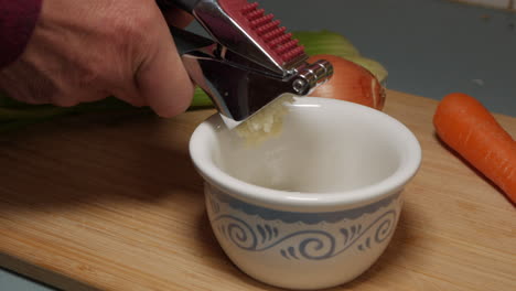 hombre presionando manualmente el ajo machacado con el uso de un utensilio de cocina moderno de acero inoxidable
