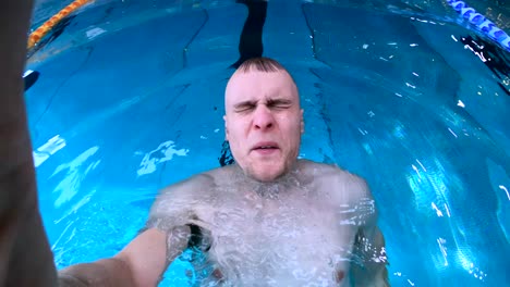 man holding breath, moving backwards submerged underwater in public indoor swimming pool